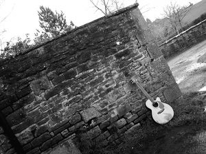 black and white photo of a guitar stood by a wall